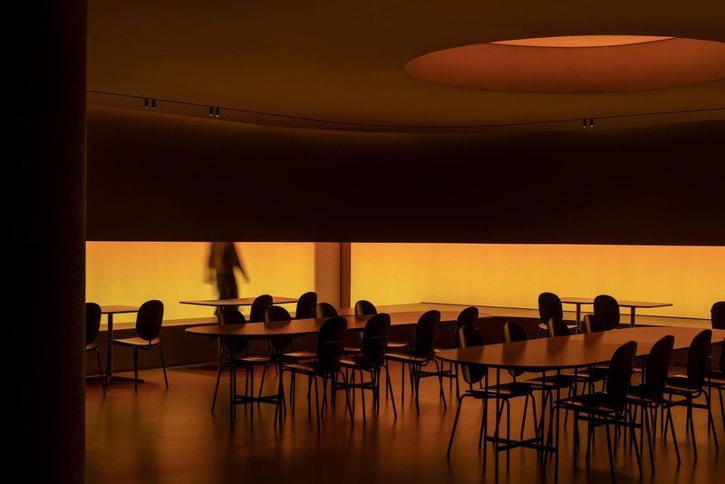 Dining area with curved ceiling oculus and backlit amber translucent wall panel with a figure passing