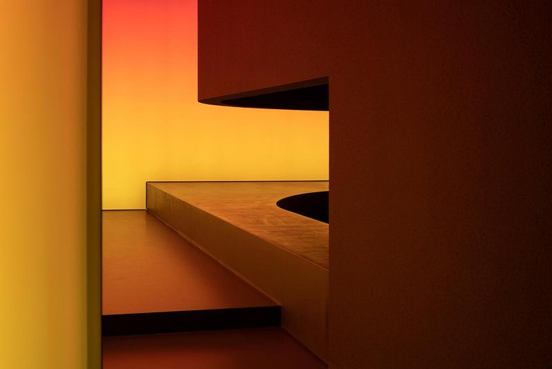 Geometric timber bench and steps beneath a glowing yellow wall panel in a recessed alcove