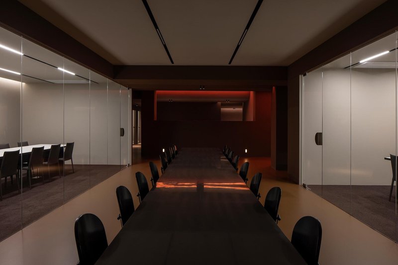 Conference table with black chairs extending toward a framed red illuminated opening