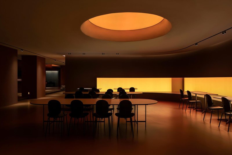 Circular skylight above dining tables arranged beside a continuous backlit horizontal window