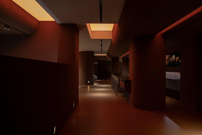 Corridor with terracotta red walls and illuminated ceiling coffers casting warm light onto the floor
