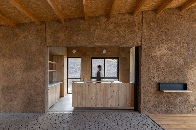View from textured panel room through doorway to kitchen counter with person in motion inside