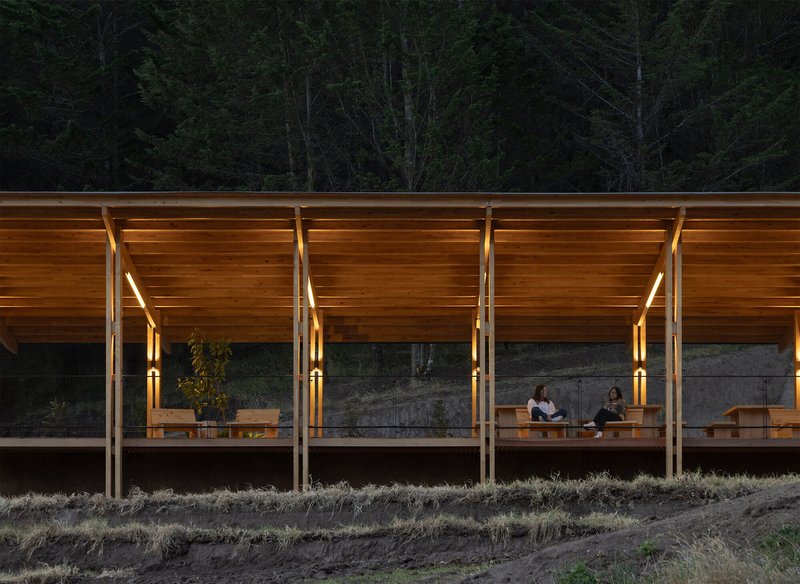 Glazed facade with timber columns and slatted soffit at dusk with two figures seated inside