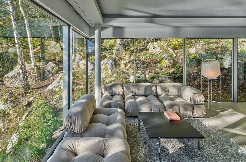 Living room with grey seating and full-height glazing overlooking the rocky wooded slope
