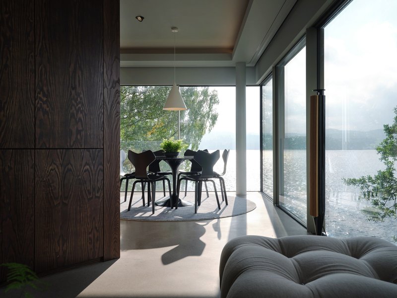 Dining area with floor-to-ceiling glass overlooking a misty lake framed by trees