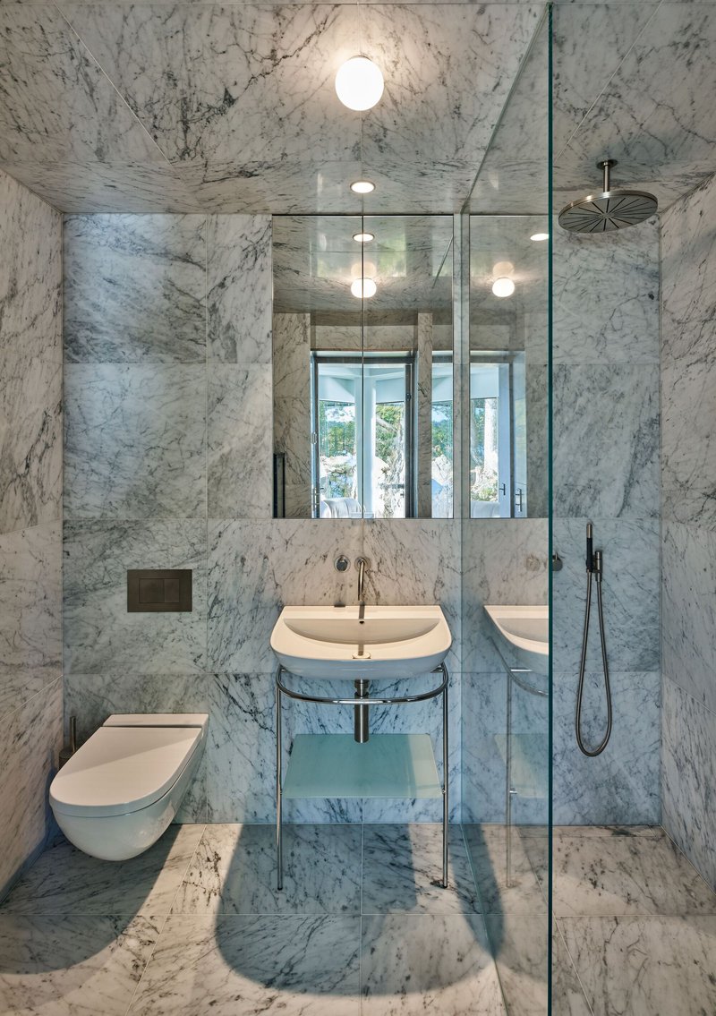 Bathroom clad entirely in white veined marble with glass shower enclosure and globe pendant lights