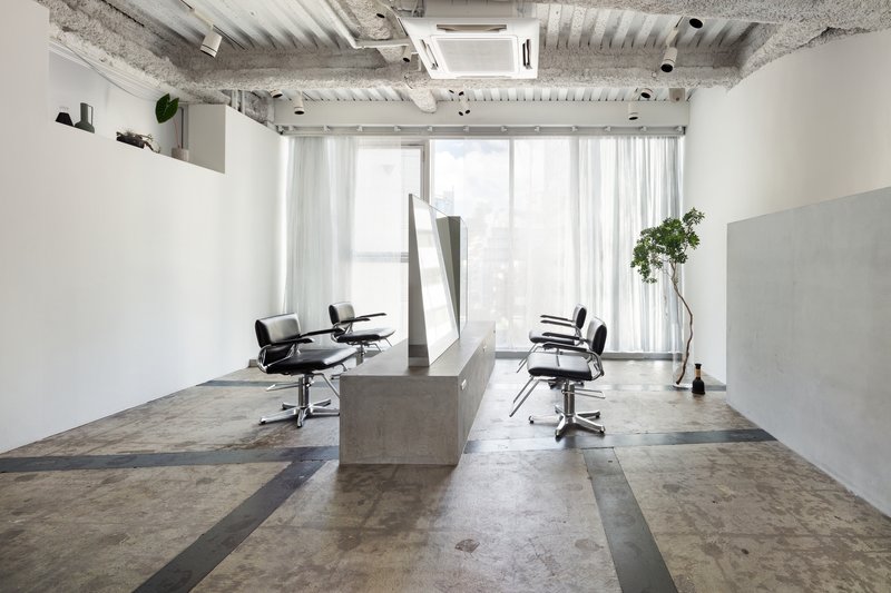 Salon workspace with concrete stations and sheer curtains filtering light from the window wall