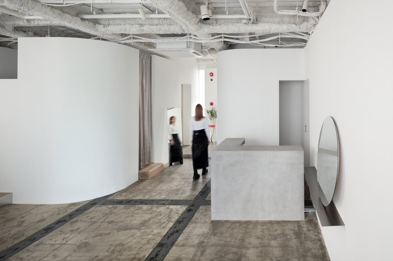 Concrete reception desk with two stylists in motion beneath exposed mechanical systems