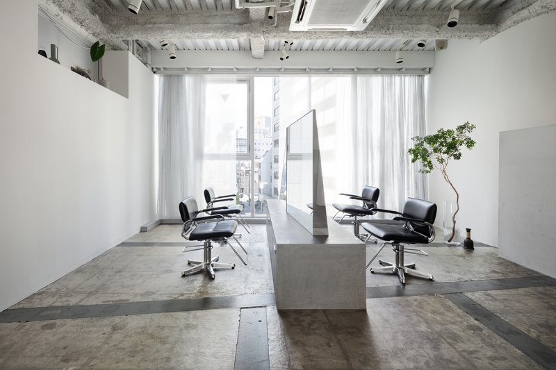 Salon interior with concrete island and floor-to-ceiling windows overlooking adjacent buildings