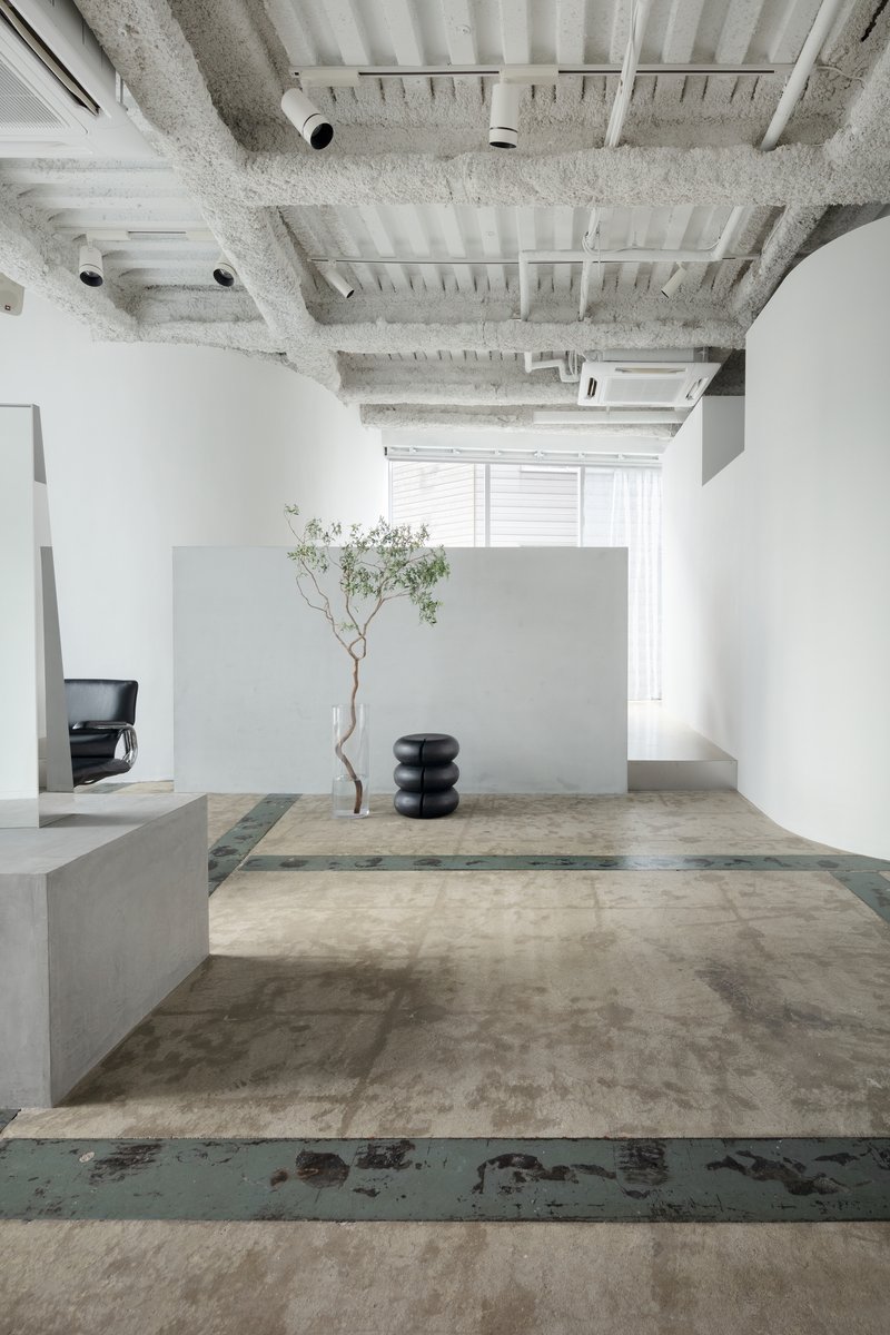 Salon platforms with layered concrete surfaces, decorative tree, and exposed ribbed ceiling with mechanical systems