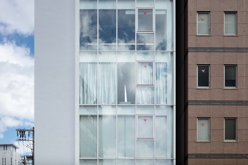 Close view of the glazed facade showing floor-to-ceiling windows with sheer curtains and red signage