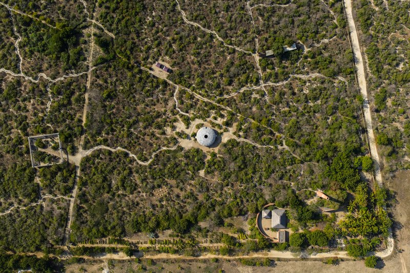 Aerial view showing two circular structures connected by dirt paths through dense scrubland vegetation