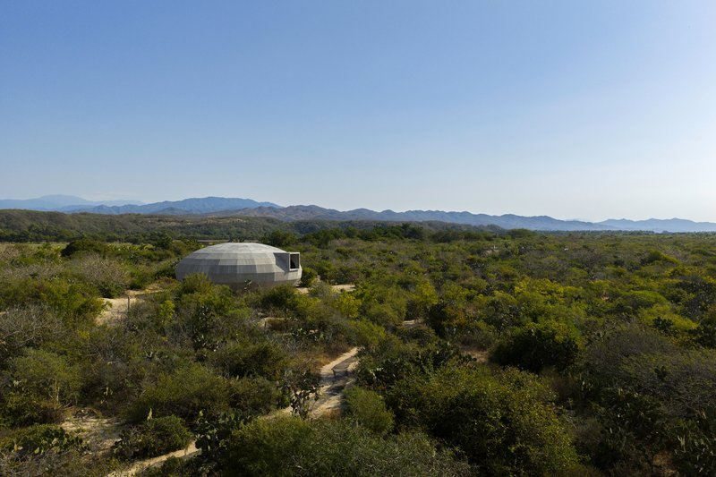 Domed concrete structure nestled in arid landscape with distant mountain ranges under clear sky