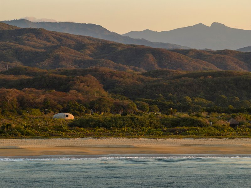 Distant view of the dome from the beach at golden hour with layered mountains beyond