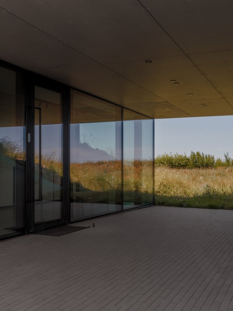 Covered timber deck with sliding glass doors opening to a grassy hillside at dusk