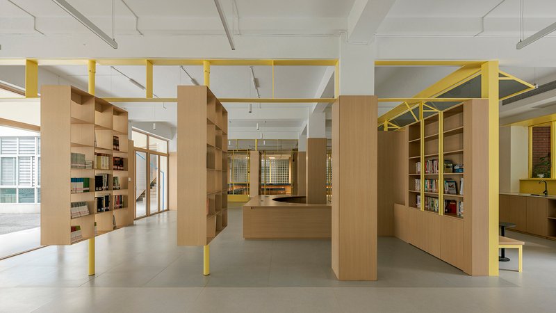 Interior library space with freestanding timber shelving units and yellow steel frames under exposed ceiling beams