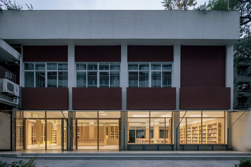 Street-facing facade with alternating bands of dark brick panels and full-height glazing at dusk