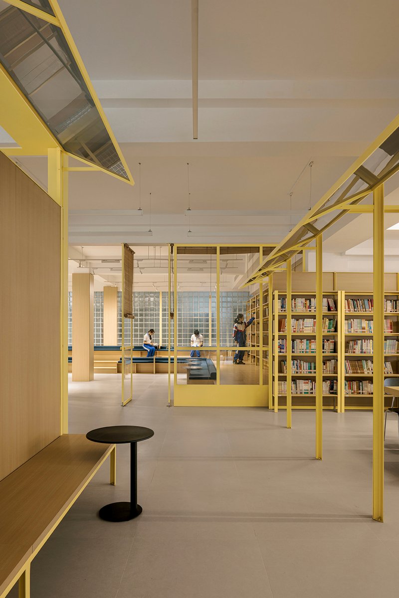 Reading area framed by yellow steel columns and beams with visitors seated on benches beneath pendant lights