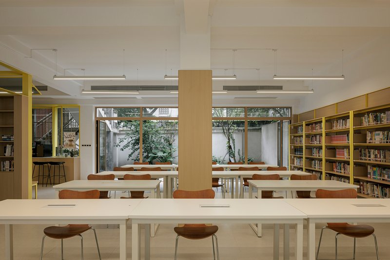 Reading room with white tables and timber stools facing courtyard windows framed by planters and trees