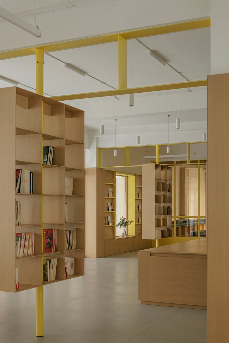 Light timber shelving units beneath yellow steel portal frames with cylindrical pendant fixtures overhead