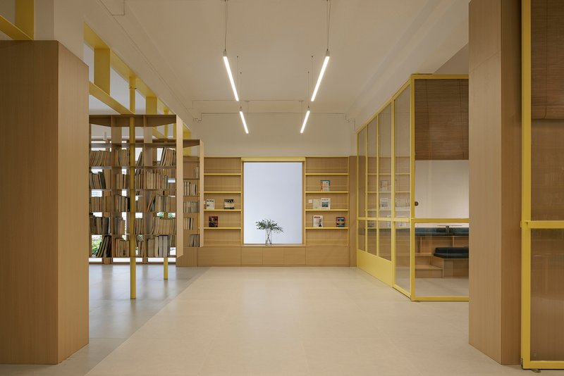 Library interior with yellow metal frame shelving and timber cabinetry under linear ceiling lights