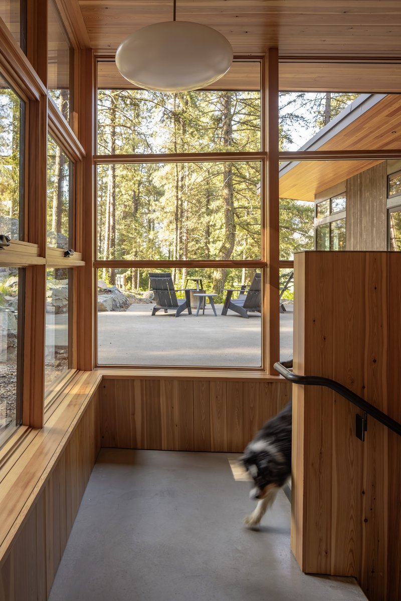 Wood-paneled interior corner with floor-to-ceiling glazing framing a view of the terrace and forest