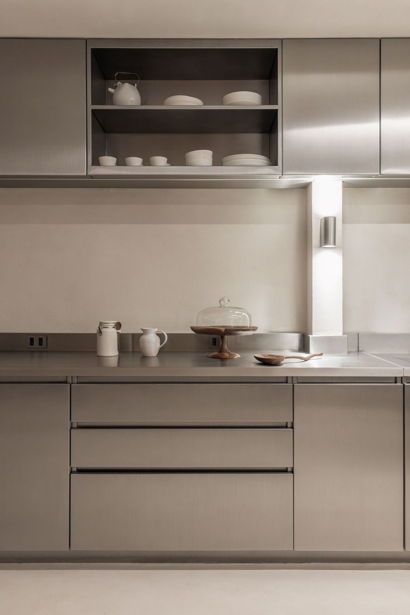 Stainless steel countertop with open shelving displaying ceramic vessels and a recessed task light
