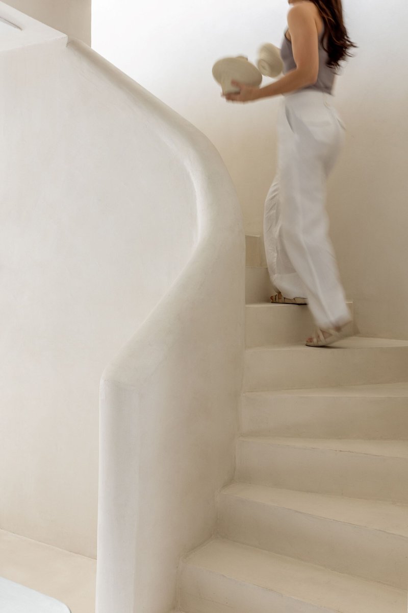 Curved plaster staircase with integrated handrail as a person ascends carrying a vase