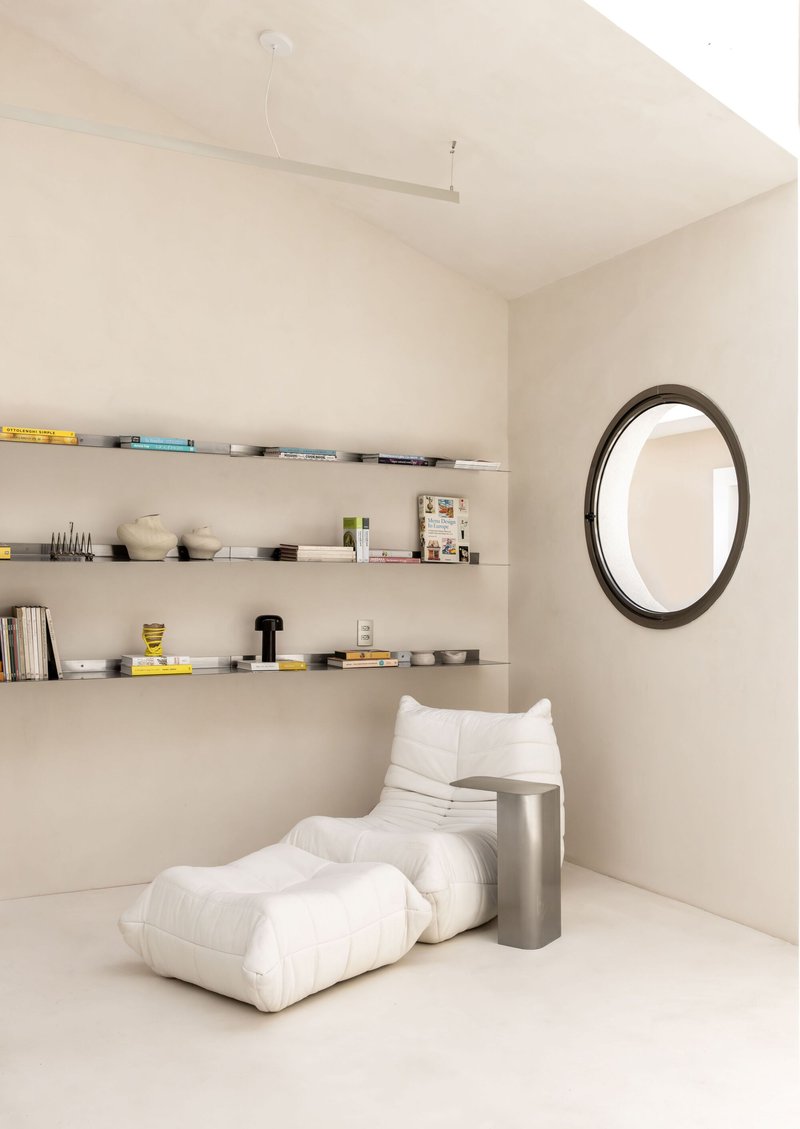 Corner nook with floating shelves and white lounge seating beneath a vaulted ceiling
