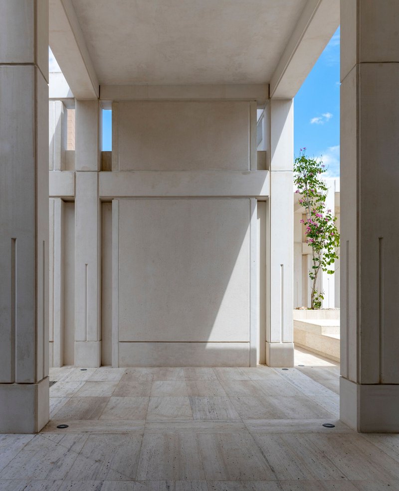 Stone passage framing a vertical slot of sky and a flowering vine at the threshold