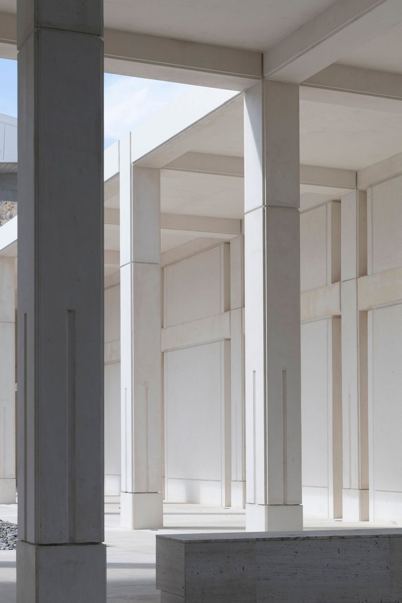 Colonnade of slender white concrete columns between cream-colored wall panels under bright daylight