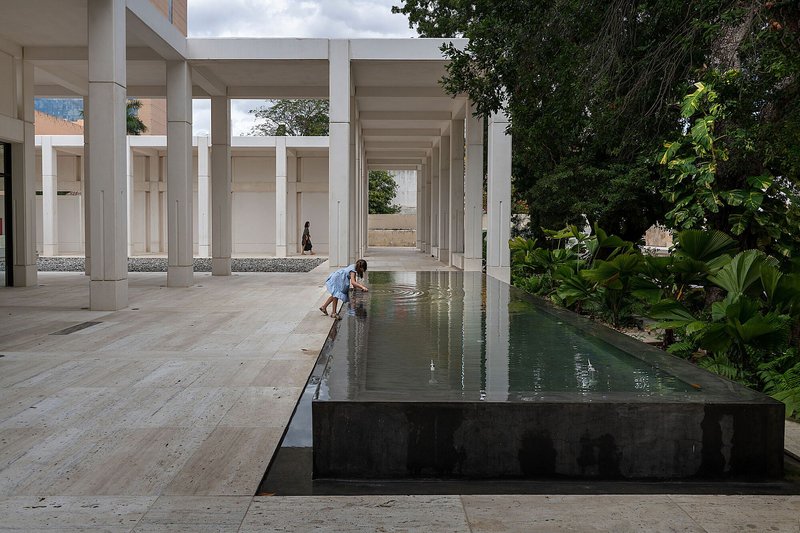 Colonnade courtyard with raised reflecting pool bordered by tropical plantings and a child at the water's edge