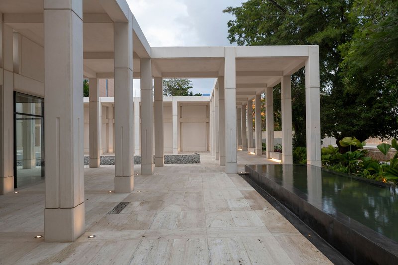Covered colonnade with stone pavers alongside a reflecting pool at dusk with lotus plants visible