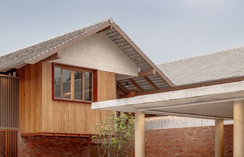 Gabled timber and tile structure elevated on concrete columns above red brick base wall
