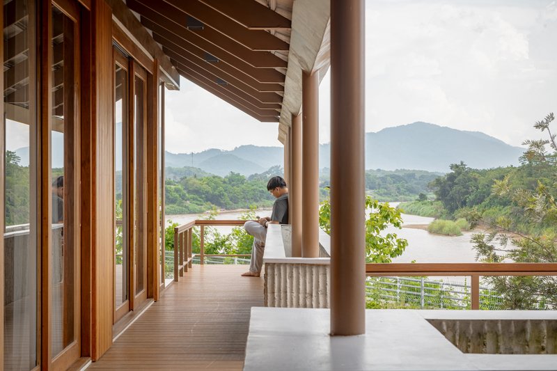 Covered timber deck with round columns and exposed rafters overlooking river and distant mountains