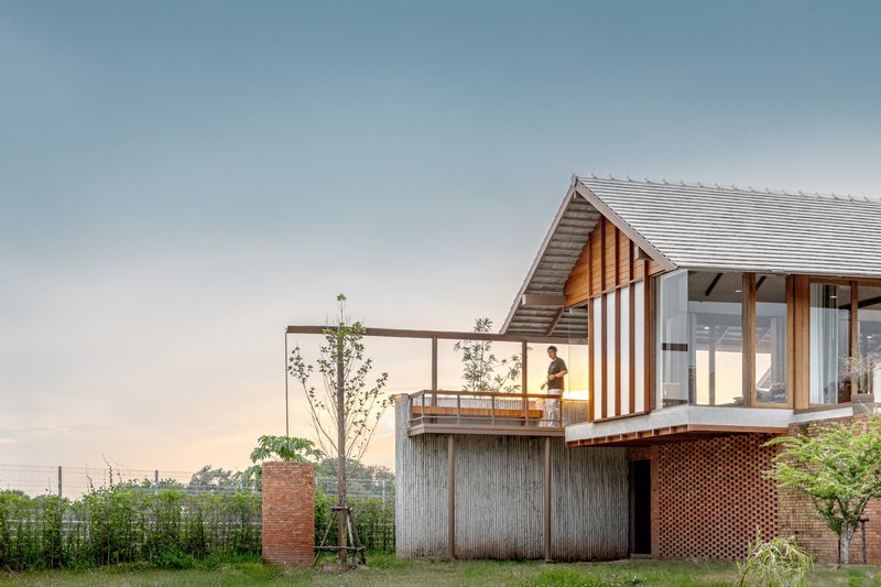 Elevated timber pavilion on perforated brick and concrete base with person on balcony at dusk