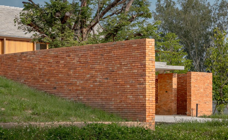 Angled brick wall with recessed joint pattern and perforated brick opening behind mature trees