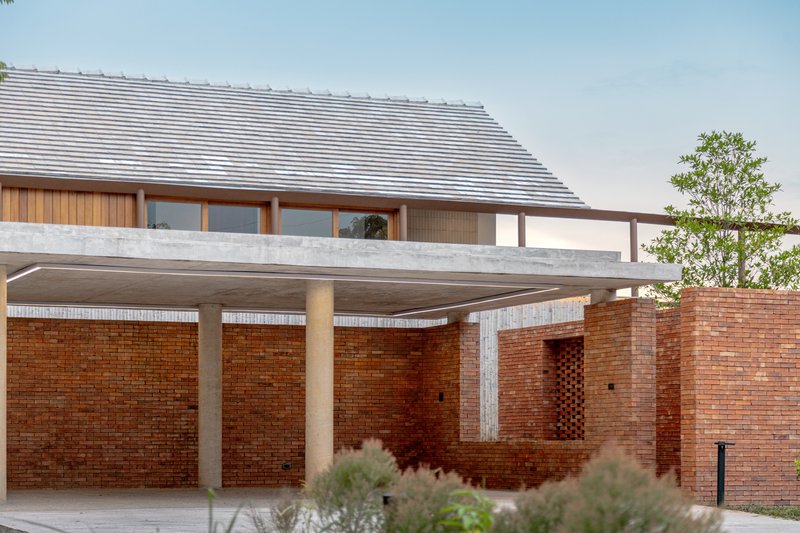 Covered carport with cylindrical concrete columns supporting a broad roof slab above brick walls