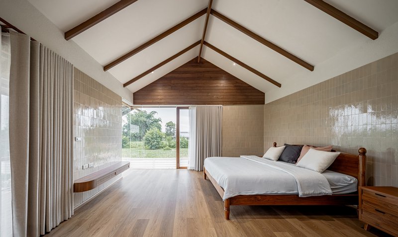 Bedroom interior with exposed timber rafters and sheer curtains overlooking greenery