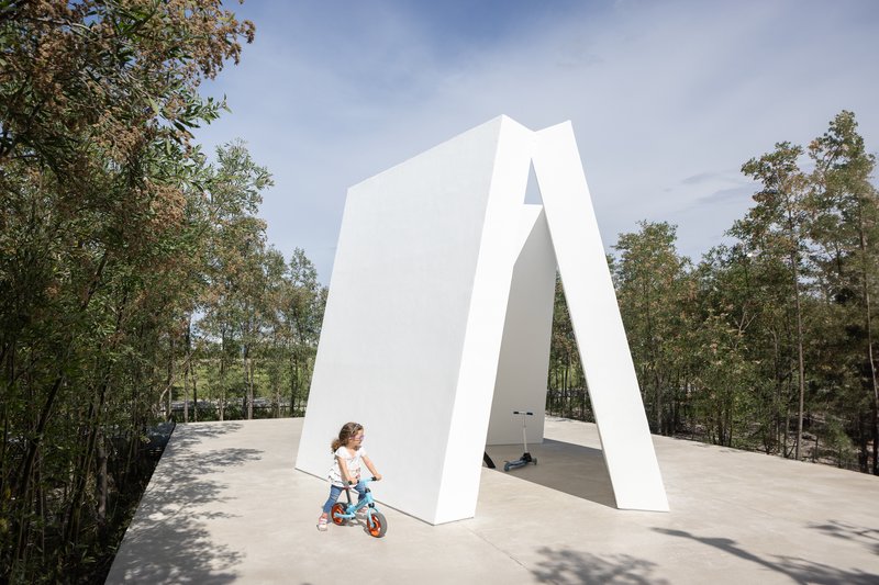 White angular portal structure framing a view through to woodland with child on bicycle