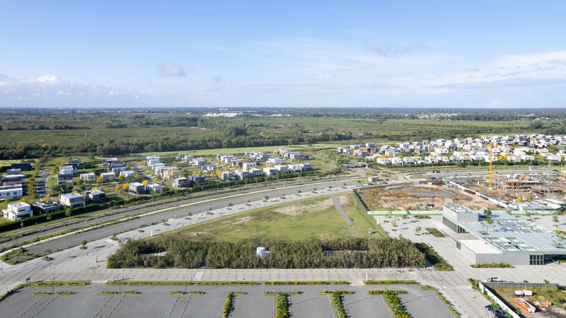 Aerial view of a residential development with scattered housing and construction zones beyond planted rows