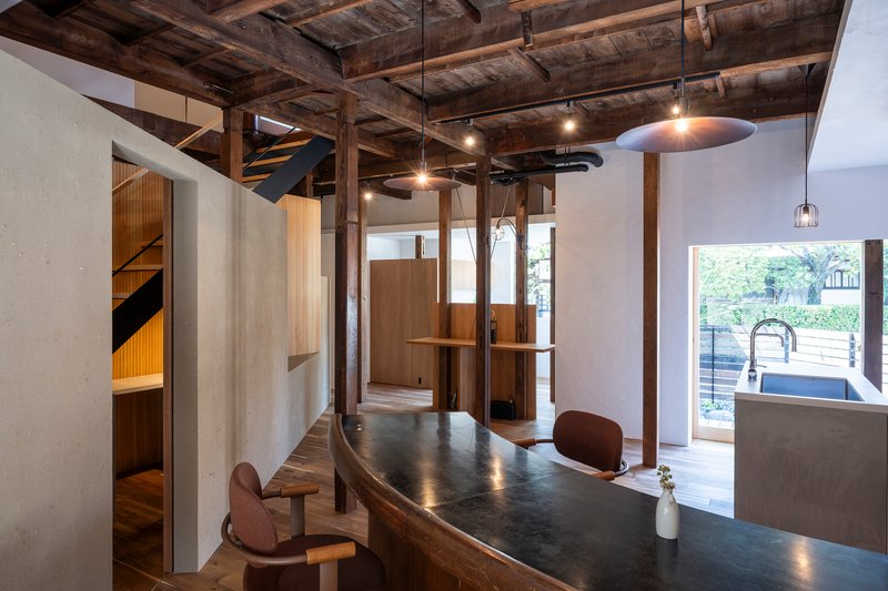 Open kitchen and dining area beneath exposed timber beams with pendant lights and doorway to terrace