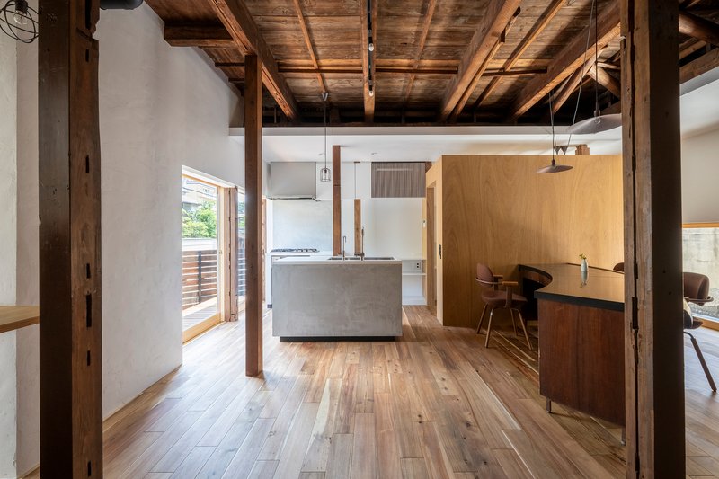 Kitchen with freestanding concrete island under heavy timber ceiling and view to exterior deck