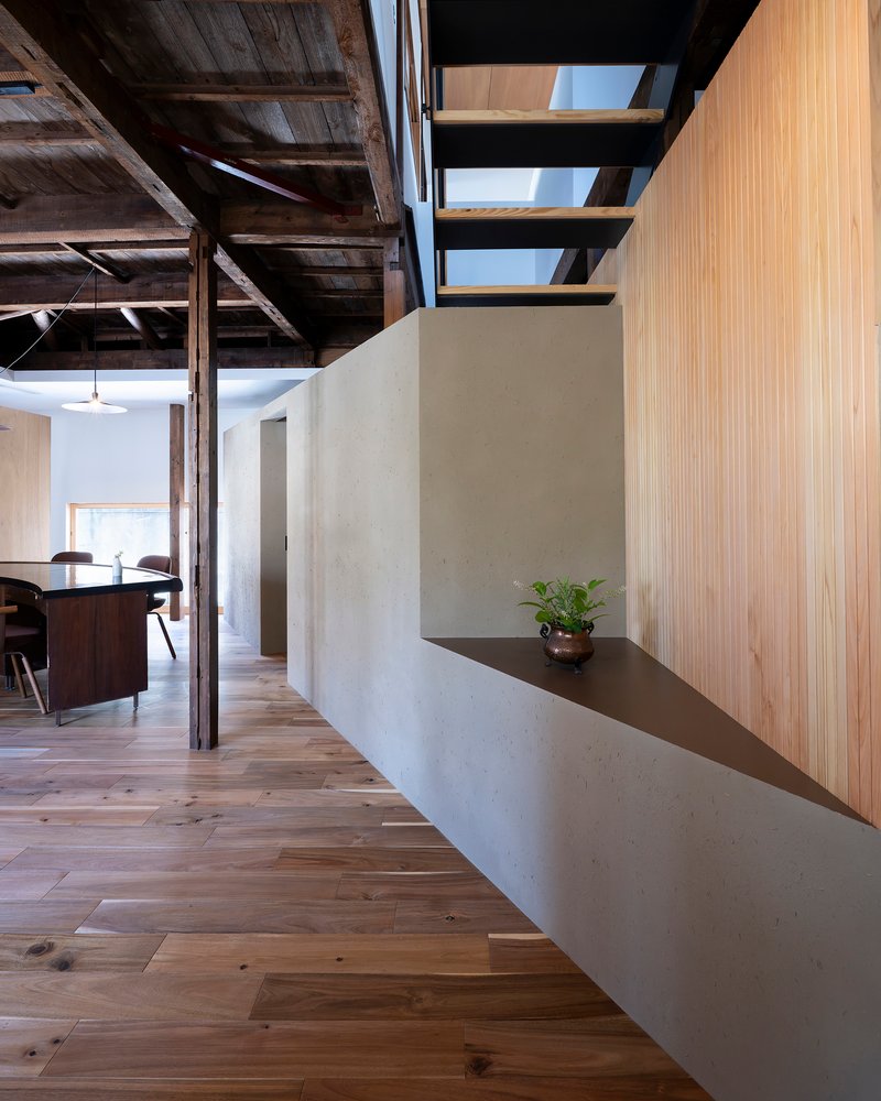 Open-tread steel staircase rising above a white plaster volume with light wood flooring below