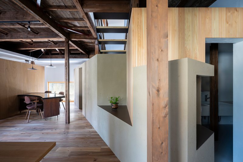White plaster wall with triangular steel shelf holding a small plant beneath timber beams