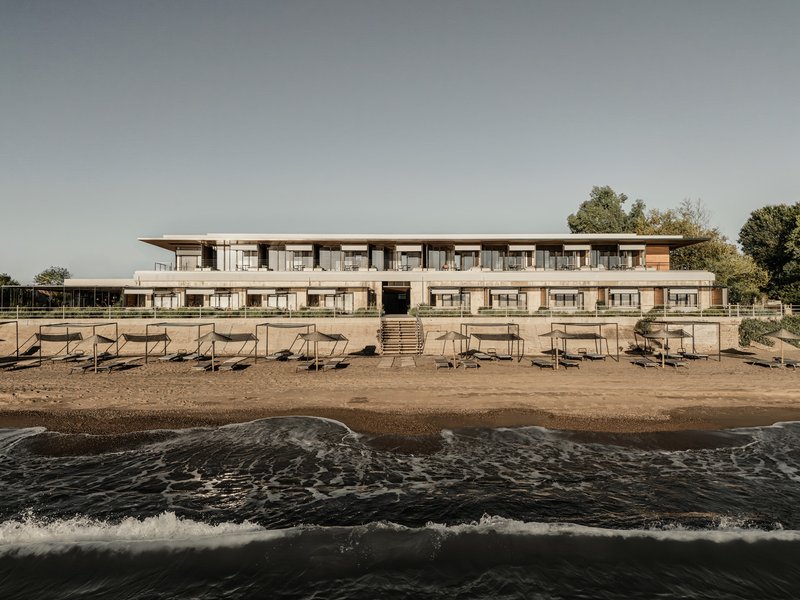 Two-story beachfront facade with horizontal balconies and timber cladding viewed from the water's edge