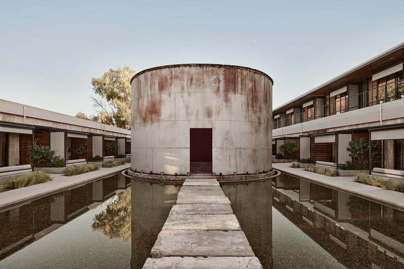 Weathered concrete cylinder with narrow walkway crossing a shallow reflecting pool in the central courtyard
