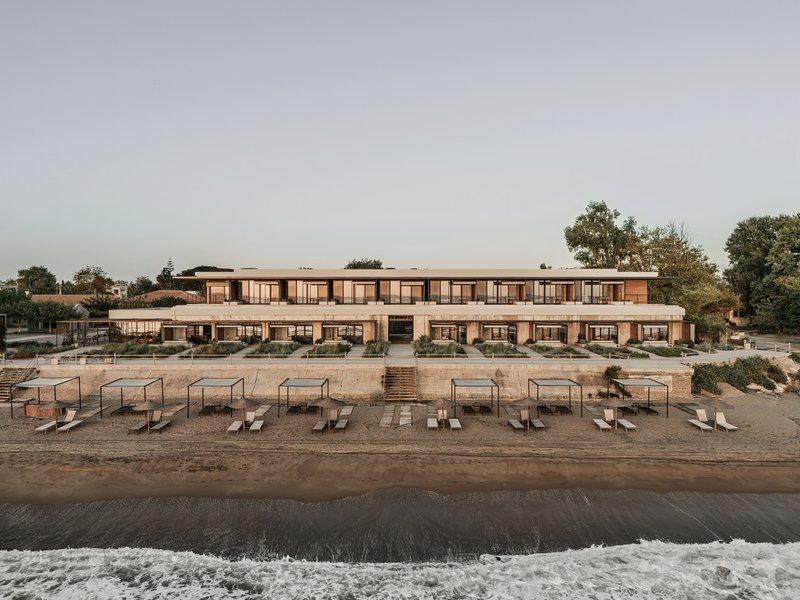 Beachfront facade with rows of lounge chairs on sand and gentle surf at dusk