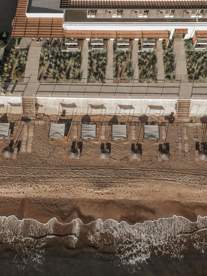 Aerial view of timber cabanas and planted terrace beds between beach and building edge