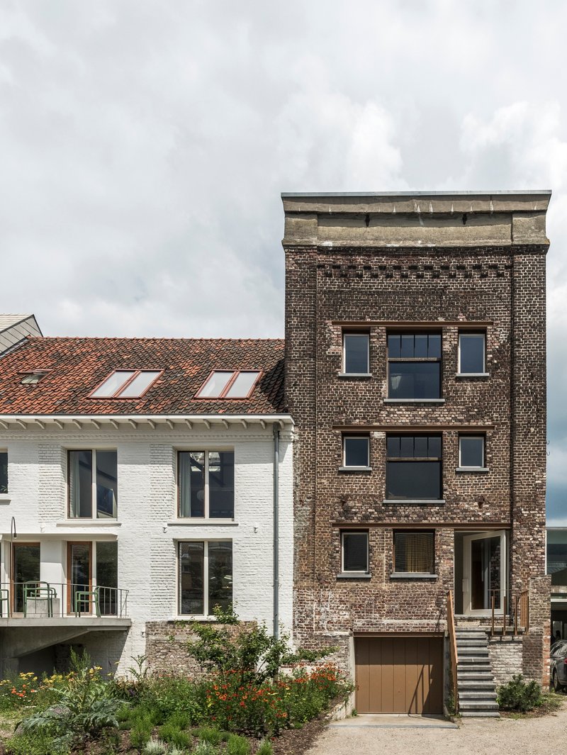 Street view showing dark brick tower adjoining a white-painted brick volume with terracotta tile roof